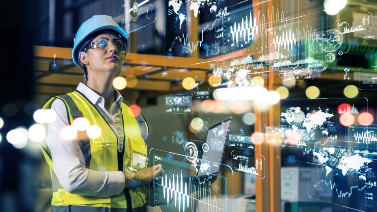 A woman in a hard hat and reflective vest interacts with virtual data screens, representing modern industrial technology.