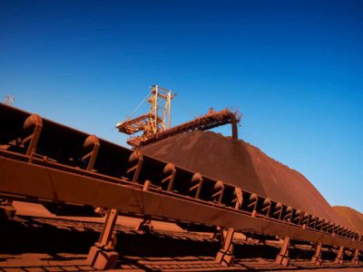 Large conveyor belt system transporting a heap of reddish-brown material under a clear blue sky.