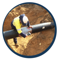 Worker in a safety helmet inspecting a black pipeline in a trench.