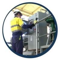 Worker operating a control panel on industrial equipment under a canopy.