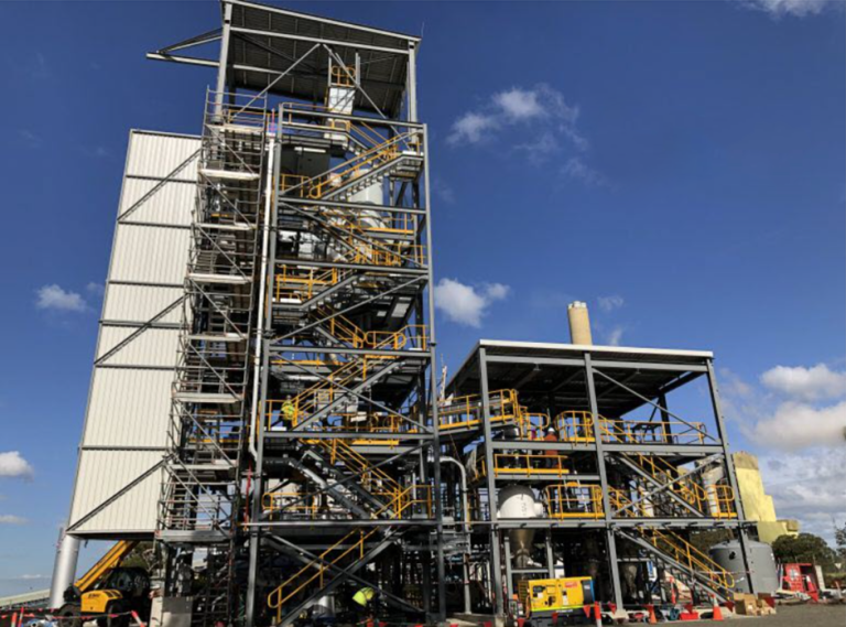 A complex industrial facility with multiple levels of metal platforms, yellow railings, and equipment, against a blue sky.