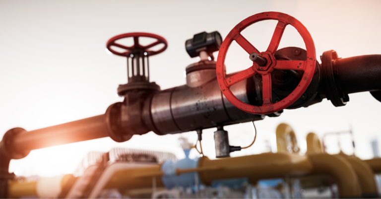 Close-up of a red valve on a large industrial pipeline with a blurred background.