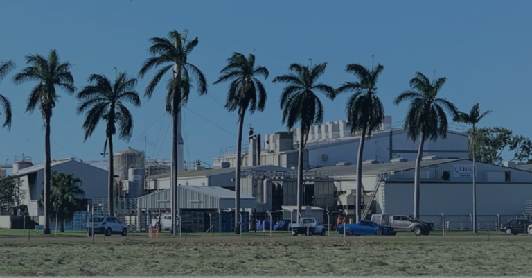 Industrial facility with palm trees in the foreground, blue sky in the background.