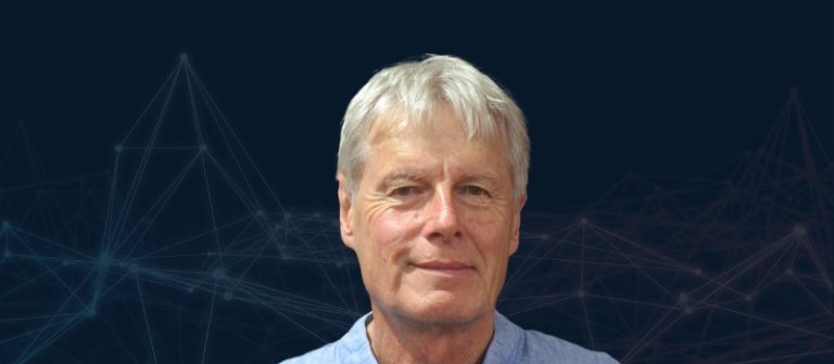 Portrait of an older man with white hair, wearing a light blue shirt, with a dark background featuring network lines.